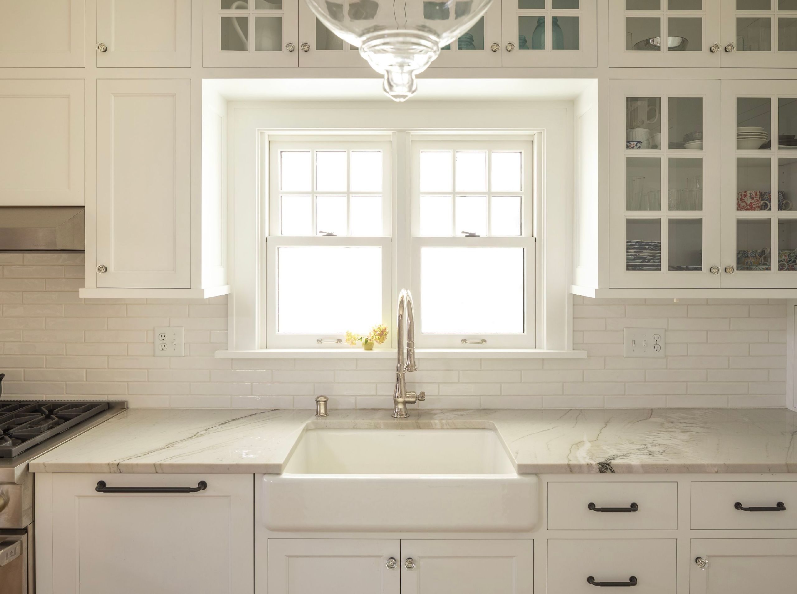white kitchen sink with paneled dishwasher and window glass upper cabinets