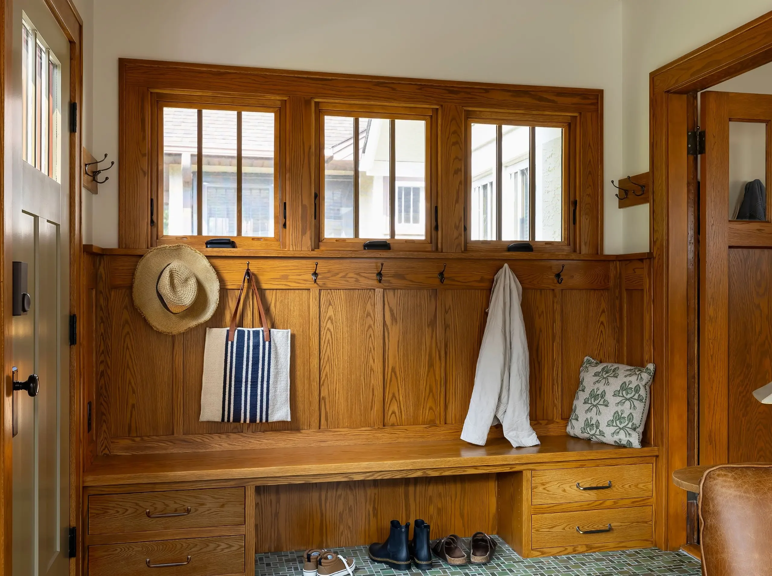 Custom oak entry bench with drawers, coat hooks and shoe storage beneath porch windows