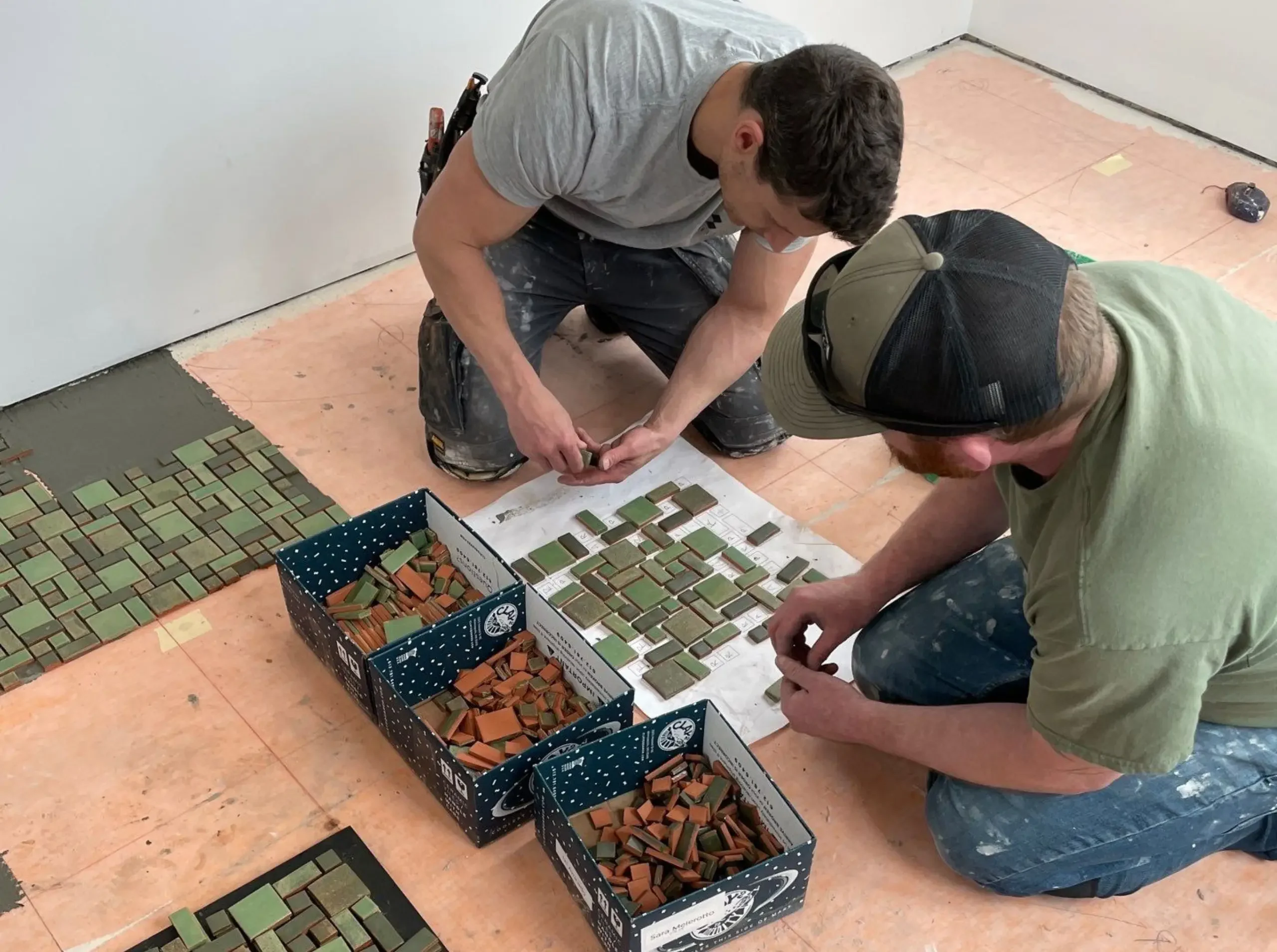 Carpenters hand-laying individual green mosaic tiles on the porch floor